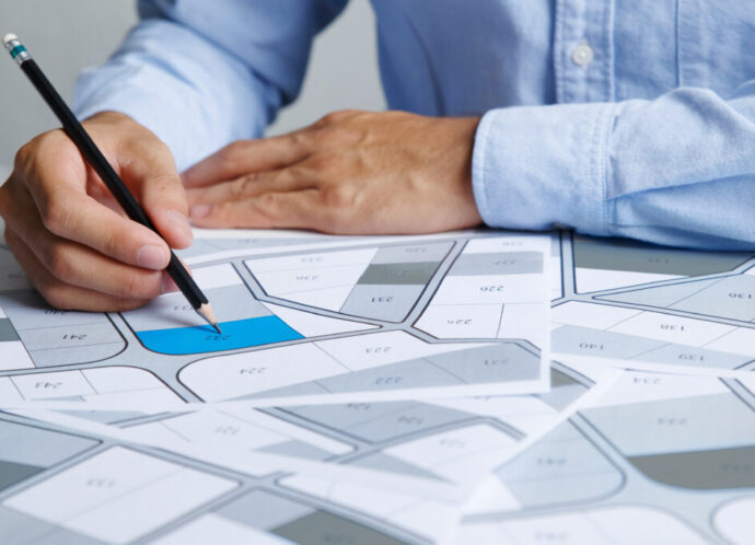 Man holding a pencil pointing to cadastral map to decide to buy land. real estate concept with vacant land for building construction and housing subdivision for sale, rent, buy, investment Man holding a pencil pointing to cadastral map to decide to buy land. real estate concept with vacant land for building construction and housing subdivision for sale, rent, buy, investment